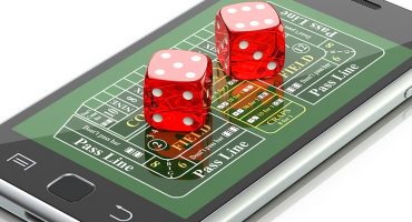 Dice sitting on top of a mobile phone displaying a craps board