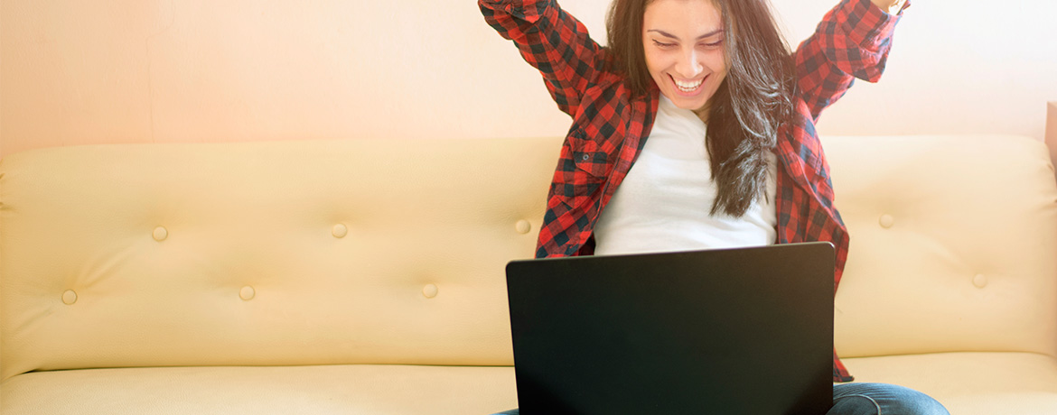 Woman raising arms over her head while looking at laptop screen